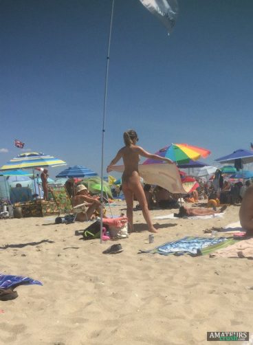 candid voyeur of teenage nudist laying her towel down on the beach